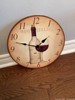 Photo of a vintage-style wall clock 14 inches in diameter with printed wine bottle and glass design on the face, black numbered dial and black clock hands.