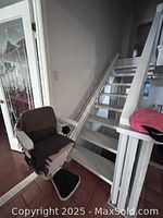 Chair lift mounted along a straight staircase, showing the full rail and the seat positioned at the staircase base.