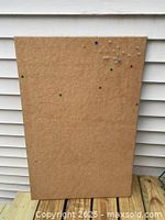 Front side of the corkboard with multiple colored pushpins in the upper right area and several pinholes visible across the surface showing use.