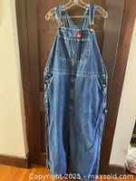 Front view of one pair of blue denim Dickies overalls hanging on hanger, showing chest pocket with logo and multiple side pockets.