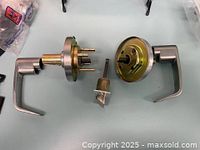 Close-up of two disassembled door handles showing lever, rose plate, spindle, and latch components on a light blue surface.