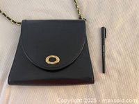Front view of black evening bag with gold-tone oval clasp and gold chain strap, placed with black pen for scale.