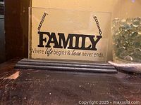 Front view of glass plaque with metal hanging word 'FAMILY' and inscription on clear glass on wood base.