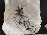 Glass starfish pendant necklace laid on white tissue paper showing full pendant and ribbon necklace.