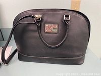 Front view of large black faux leather ladies bag with handles and attached shoulder strap.