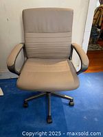Front view of light brown office chair, showing padded seat and backrest with horizontal stitching, armrests, and caster wheel base.
