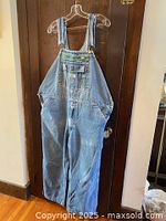 Front view of one pair of blue denim overalls hanging on a hanger showing front chest pocket and straps