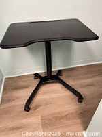 View of black adjustable rolling computer workstation table with contoured surface and recessed slot for holding a tablet or pens.