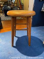 Side view of the stool showing the round seat, four straight legs, and crossbars for support. Wood finish is natural with some patina from use.