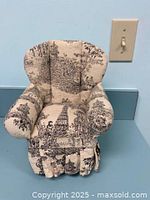 Front view of the small upholstered doll chair next to a wall light switch for size reference.