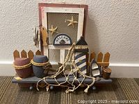Front view of the nautical themed wooden welcome sign and key rack showing decorative elements like lighthouse, pots, starfish, and netting.