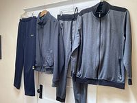 Full view of collection including gray zip-up jacket with black panels, matching pants, and navy sweatpants hanging on hooks