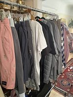Clothing rack showing various tall men's pants and shirts, including peach pants with embroidery and Reebok joggers.
