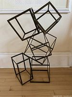 Full view of stacked metal rectangular boxes sculpture on wood floor against white wall.