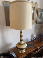 Full view of the tall Mid-Century Modern ceramic lamp with cream and chocolate brown Greek Key pattern and cream fabric shade on top of a wooden surface.