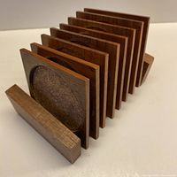 Side angled view showing seven teak wood square coasters with circular cork inlays inside a teak wood storage holder.