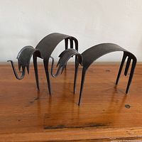 Pair of hand-crafted abstract animal sculptures made of dark metal, shown from side angle on wooden surface.