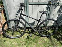 Full left side view of black Specialized bicycle showing frame, tires, seat, and pedals outdoors in sunlight.