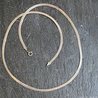 Full view of the 20 1/4 inch silver snake chain with spring ring clasp laid out on a dark surface.