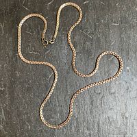 Full view of the silver chain laid flat on a dark surface showing its length and rectangular link design resembling subway tiles.