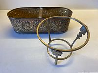 Two-piece lot showing the repousse brass planter and separate brass pot holder frame on a white surface.