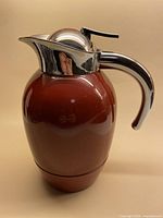 Full view of vintage burgundy thermos showing rounded body and chrome handle and lid.