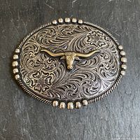 Full view of the oval metal belt buckle showing bull motif and floral scroll background with studded border