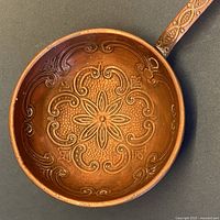 Close-up photo of the ladle bowl showing detailed repousse floral and scrollwork design.