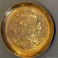 Full view of the vintage solid brass repousse plate showing overall floral and foliage embossed design and round shape.