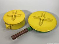 Frying pan with green base, yellow lid, and teak handle alongside yellow enamel Dutch oven with lid