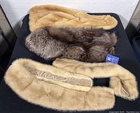 Three mink fur collars laid on black surface showing two beige shawl collars and one darker mink collar with tag.