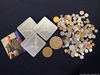 Photo of assorted coins, three silver-colored bullion bars with bird engraving, and larger vintage coins