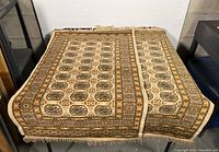 Two wool rugs folded together showing beige, brown, gold geometric floral pattern with fringed edges.
