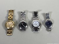 Four wristwatches laid flat showing front faces and metal bands: gold-tone Swatch Irony Diaphane Full Blooded Chronograph, silver Victorinox Swiss Army, silver Swatch chronograph, blue dial Freelook chronograph