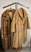 Two full-length mink fur coats hung side by side against a wall
