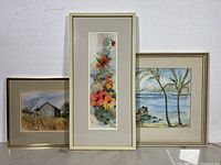 Three framed watercolour paintings shown together on wall: vertical floral, seascape with palm trees, rural barn scene