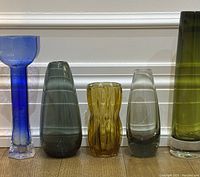 Five vases lined up showing varying heights, colors, and styles including blue, smoked green, amber, and clear glass pieces.