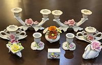Full set of porcelain Dresden candleholders, matchbox holder, and flower vase showing all items together on a table.