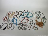 Overview of various beaded necklaces and bracelets laid on white background showing different colors and stones.
