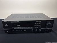 Front view of the Denon AVR-1100 AV surround receiver showing power button, display, volume knob, headphone jack, and function buttons.