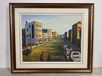 Framed signed oil painting showing urban street with buildings, parked cars, and two figures