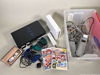 Full lot overview with Nintendo Wii console, Sony PS2 console, controllers, game discs, cables, and glasses case