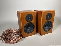 Pair of Linn Tukan teak veneer bookshelf speakers on white background with coiled speaker cables