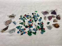 Wide view of entire stone collection spread on white cloth showing polished and raw stones in blue, green, purple, clear, red and brown hues