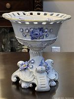 Front view of the Dresden Von Schierholz porcelain compote bowl showing detailed blue flower bas-relief and gilded accents on pedestal and bowl.