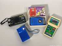 Set of four vintage electronics: black and yellow Dynamo & Solar radio flashlight, blue Setico AM pocket radio with box, royal blue Emerson AM radio, and cream-colored Coleco Quarterback handheld game