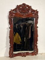 Front view of vintage wall mirror showing the ornate carved wooden frame and beveled mirror glass. Reflective surface and wood details clearly visible.