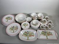 Full set arranged on table showing all dinnerware and serveware pieces including plates, bowls, cups, saucers, and trays with visible colorful fruit tree motif and red trim.