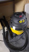 Full view of yellow and black Shop Vac with hose coiled around the base, showing overall condition and included accessories.