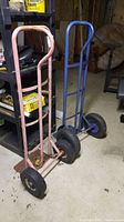 Pink metal hand cart with solid wheels and blue metal hand cart with large pneumatic tires side by side in storage area